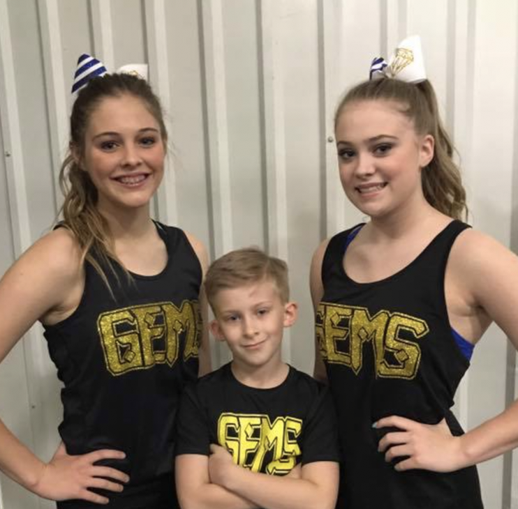 two girls and a boy in cheer team attire smiling at the camera